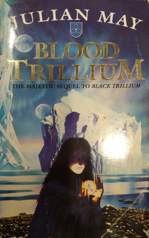 Cover of Blood Trillium by Julian May. A woman in a violet cloak holds a glowing orb before a background of the ocean and large ice platforms.