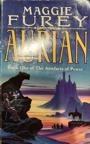 The cover of Aurian by Maggie Furey, Book One of the Artefacts of Power. In the foreground is a traveller holding up magical light orbs that hover above their palm, before a gargoyle of a lion. In the middle ground is a lone horseman standing surveying an army leading into the distance where a castle stands lone atop a mountain, with desert dunes surrounding it. Visual contrast between the castle and mountains is achieved by blue and purple tints while the dunes are bright yellow and orange, conveying an overall mystical feeling.