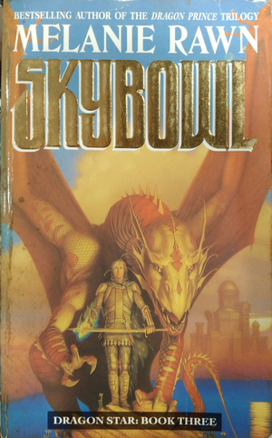 Cover of Skybowl by Melanie Rawn. Book three in the Dragon Star series. A knight holds a sword in both hands with a yellow dragon behind him. They are standing on a cliff with an water view behind them and buildings across the waterfront visible in a hazy background.